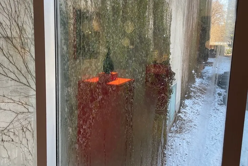 The image shows a view through a wet glass pane with water droplets looking out to a red table with orange items on it and a snowy scene outside