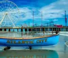 A colorful boat labeled Atlantic City sits on the shore with a large Ferris wheel and an amusement park on a pier in the background