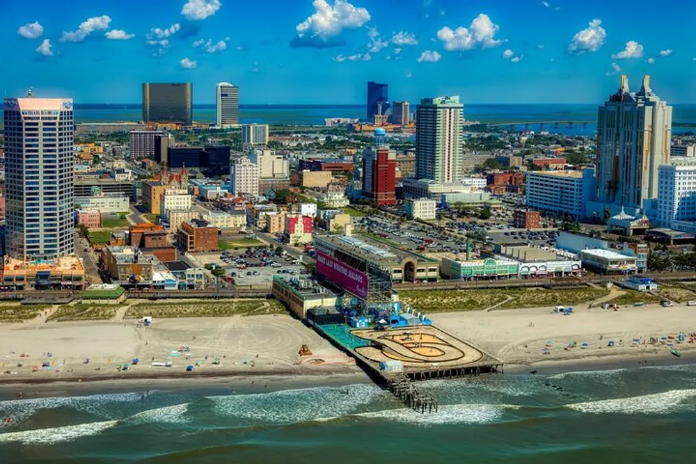 This image shows an aerial view of a vibrant coastal city with a sandy beach in the foreground a pier extending into the sea and a downtown skyline under a clear blue sky