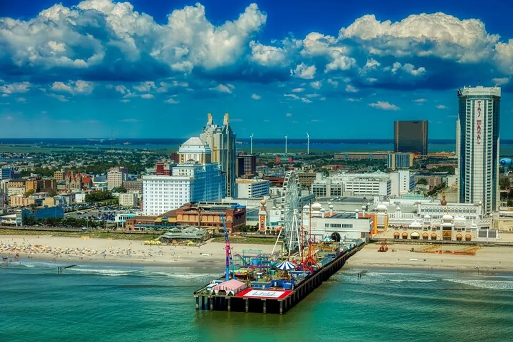 This image shows a vibrant aerial view of a coastal city with a pier amusement rides a sandy beach and a clear blue sky with fluffy clouds
