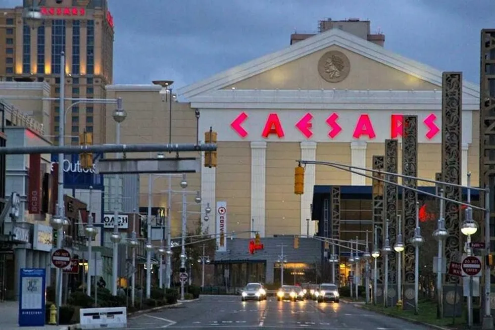 The image shows an overcast city street leading towards the large prominently signed entrance of the Caesars casino and hotel complex under a twilight sky