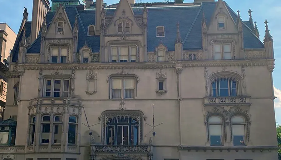 The image shows a grand, ornate building with Gothic Revival architectural features under a clear blue sky.