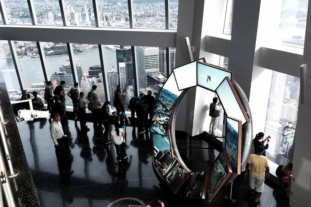Visitors enjoy a panoramic city view from a high vantage point with large windows while a person interacts with an installation featuring reflective surfaces