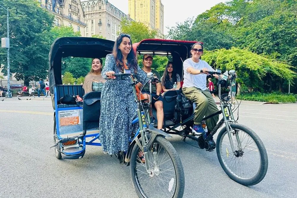Four people are enjoying a ride through a park on a pedicab smiling and posed for the photo