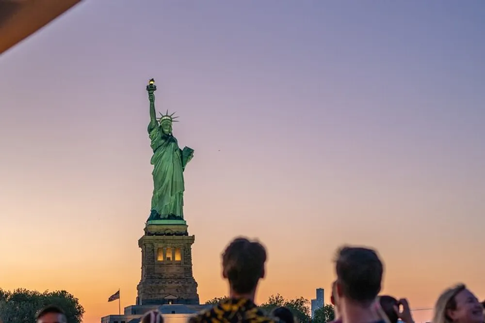 The image captures a serene evening with people gazing at the Statue of Liberty against a dusky sky