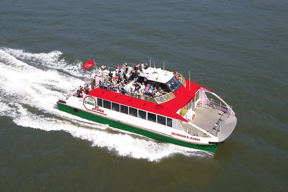 A group of passengers is enjoying a sunny day on an open deck of a red and green Circle Line sightseeing boat cruising on the water