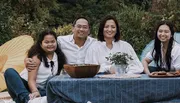 A family of four is smiling and enjoying an outdoor meal together.