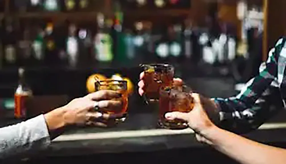 Three people are toasting with whiskey glasses at a bar