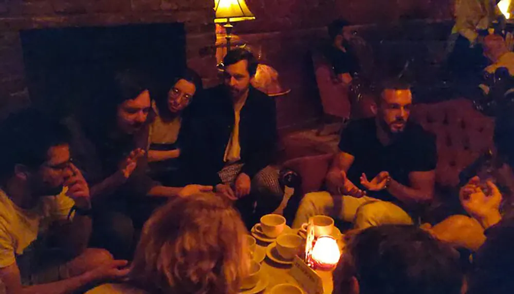 A group of people appear to be engaged in a relaxed and intimate conversation in a dimly lit room with a candle on the table