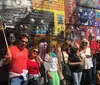 A group of smiling people is posing in front of a colorful mural with various portraits and graffiti art