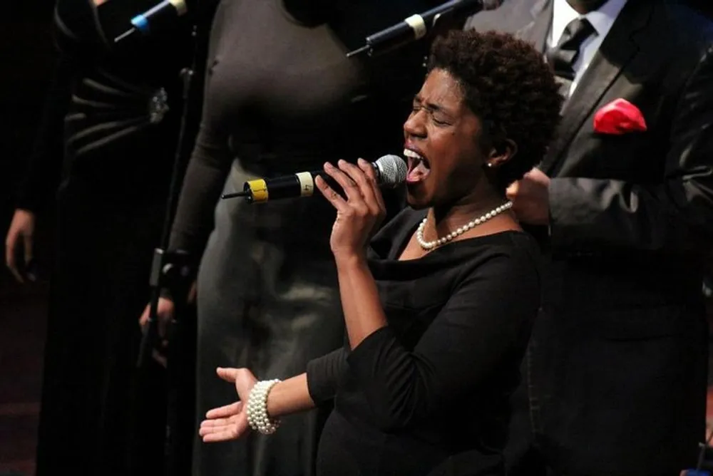 A woman passionately sings into a microphone with a choir in the background