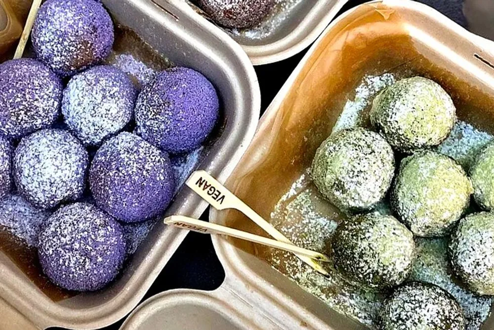 The image shows two trays of colorful dusted truffles one purple and one green with a wooden utensil labeled VEGAN