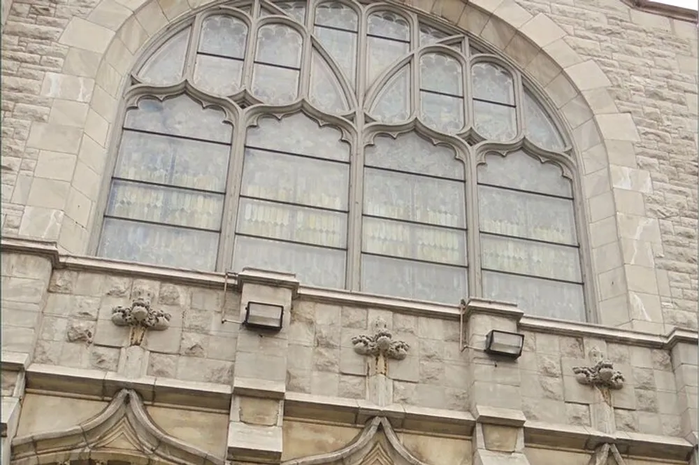 The image shows a large ornate gothic-style window with stained glass set in a stone building with decorative stonework detailing
