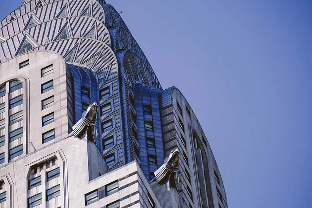 The image depicts the upper section of an Art Deco skyscraper with distinctive terraced crown and decorative metalwork against a clear blue sky