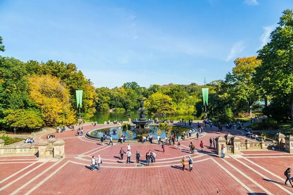 This image shows a bustling Bethesda Terrace overlooking the Bethesda Fountain in Central Park New York City with people enjoying a sunny day amidst the changing colors of autumn leaves