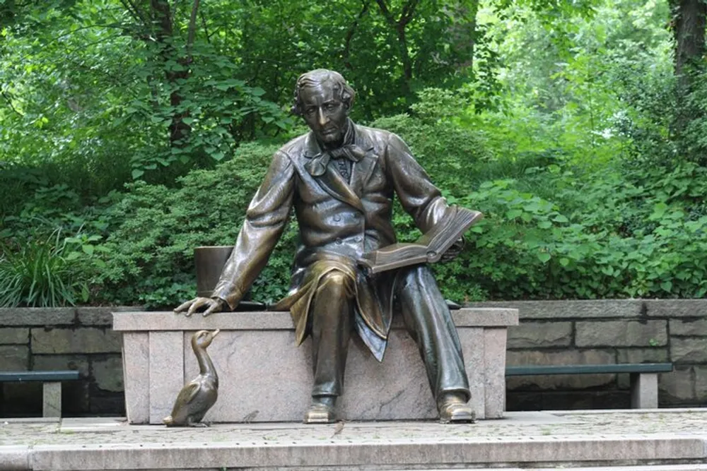 The image shows a bronze statue of a seated man holding an open book with a duck at his feet set against a backdrop of lush greenery