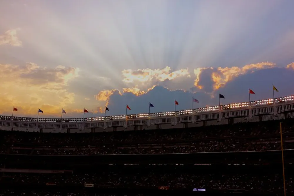 The image shows a dramatic view of sunlight radiating through clouds above a stadium adorned with various flags creating a beautiful and ethereal atmosphere