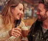 A woman and a man are smiling and toasting with drinks in a warmly lit setting