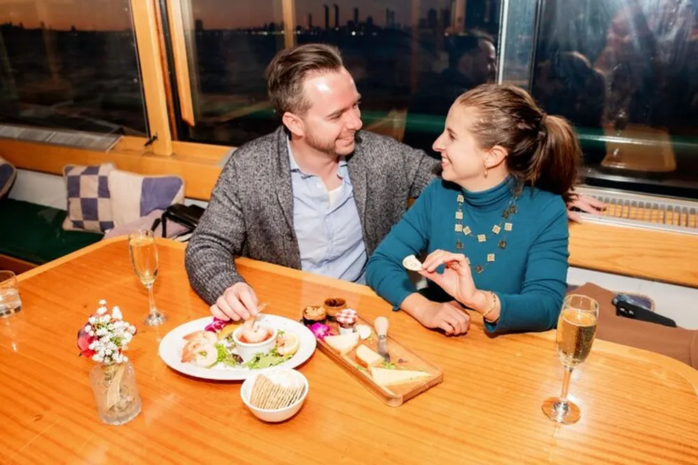 Two people are sharing a delightful moment over a meal and drinks at a table with a view out the window