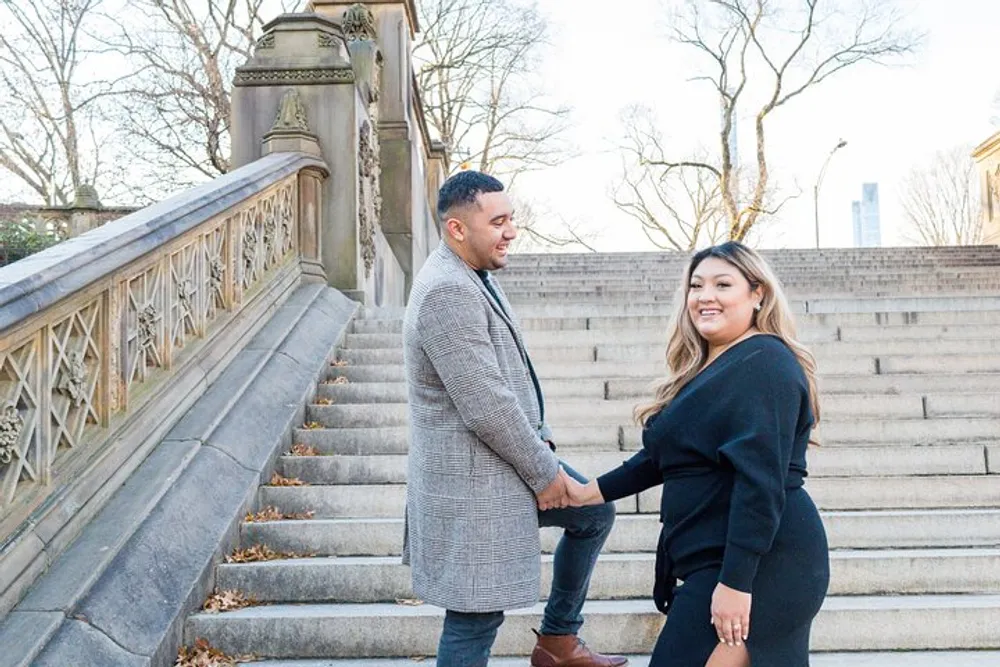 A smiling man and woman hold hands on a staircase outdoors sharing a joyful moment together