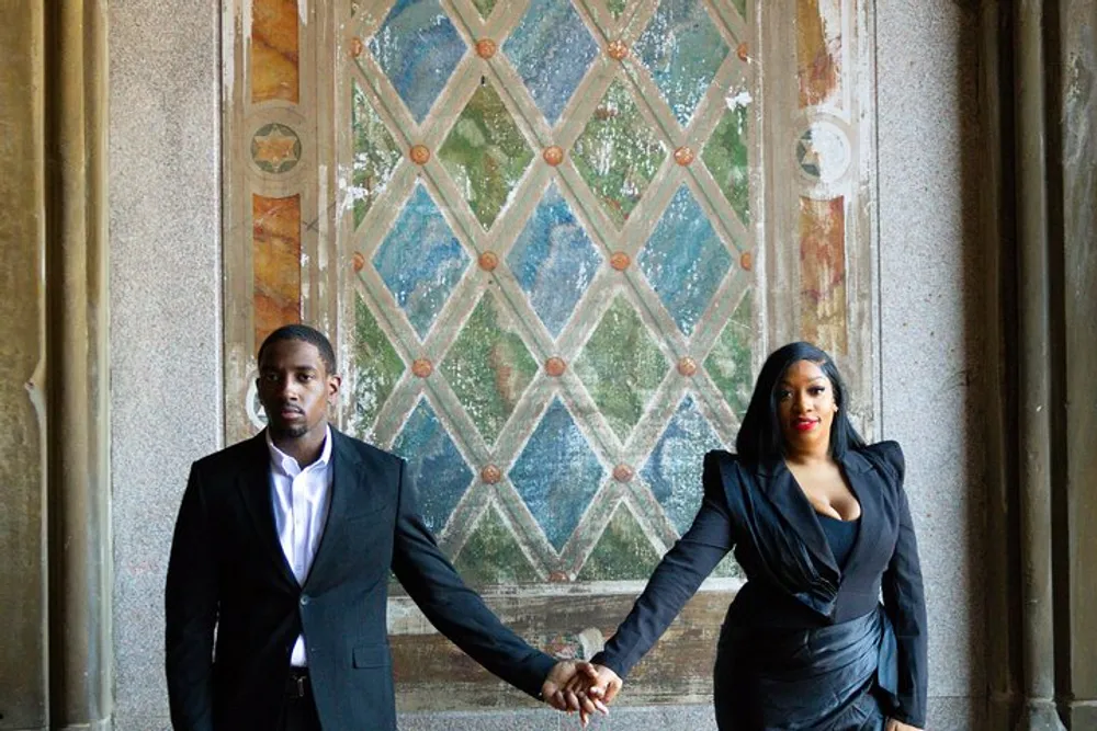 A man and woman dressed in formal attire are holding hands in front of an ornate weathered door