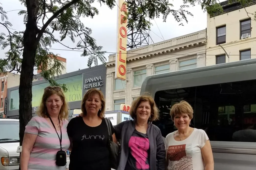 Four women are smiling in front of the iconic Apollo Theater marquee