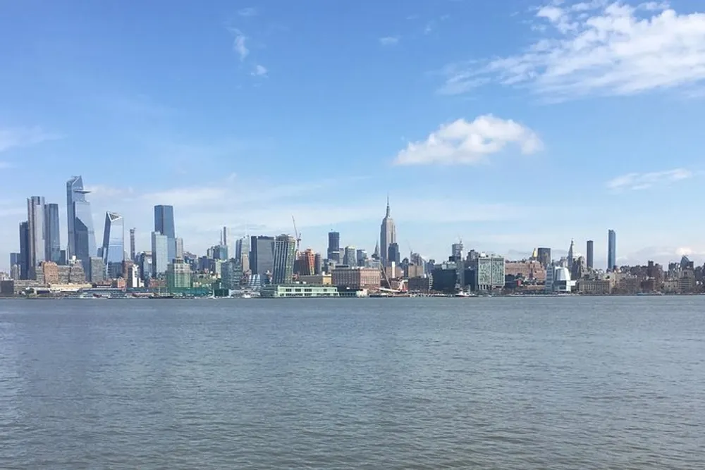 This image shows a daytime view of a city skyline from across a body of water under a partly cloudy sky