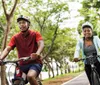 Two people wearing helmets are riding bicycles along a tree-lined path
