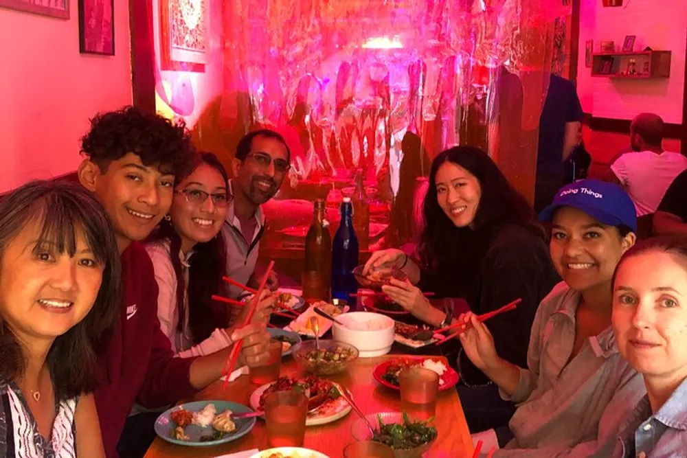 A group of people are enjoying a meal together at a restaurant bathed in pink lighting