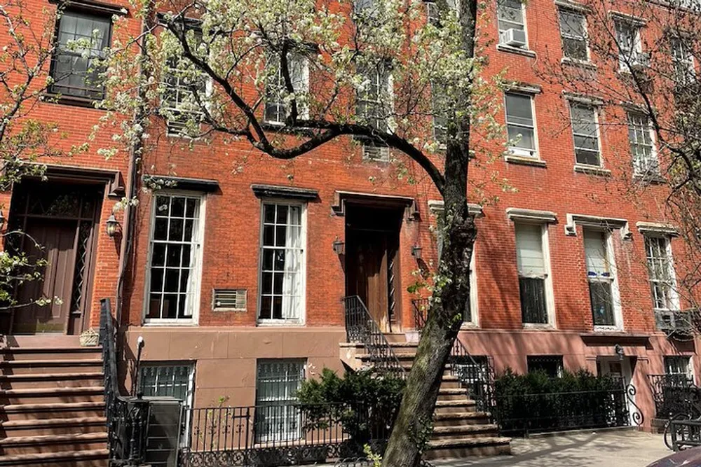 The image displays a charming red brick residential building with classic features flanked by a blossoming tree presumably located in an urban area with a tranquil atmosphere