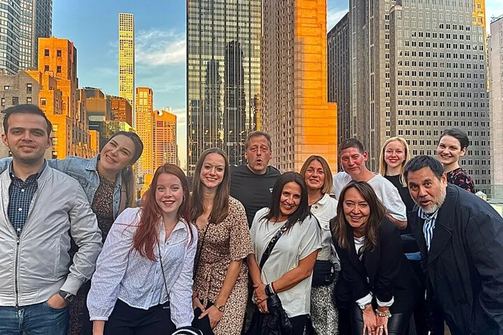 A group of people poses for a photo with a backdrop of towering urban buildings displaying a blend of smiles and amusing expressions