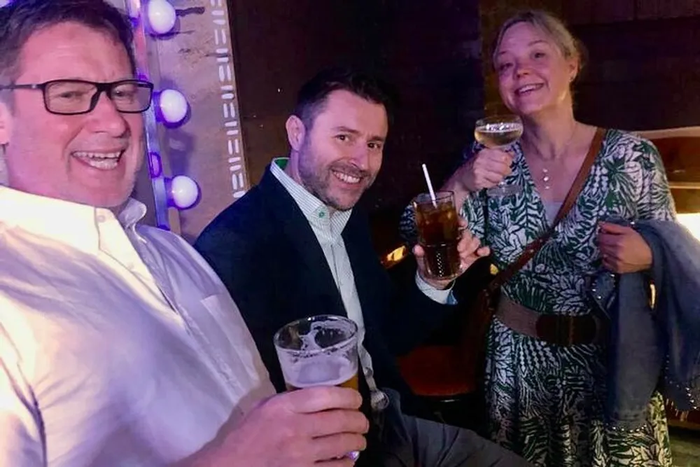 Three smiling people are toasting with drinks at a social gathering