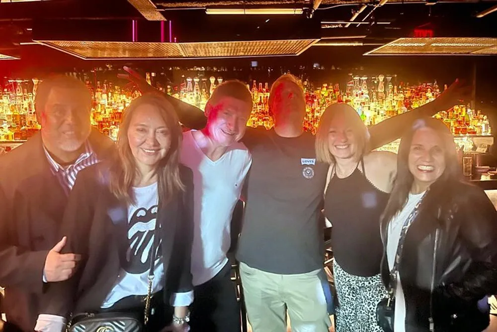 A group of five smiling people pose for a photo together in front of a bar illuminated by warm lights