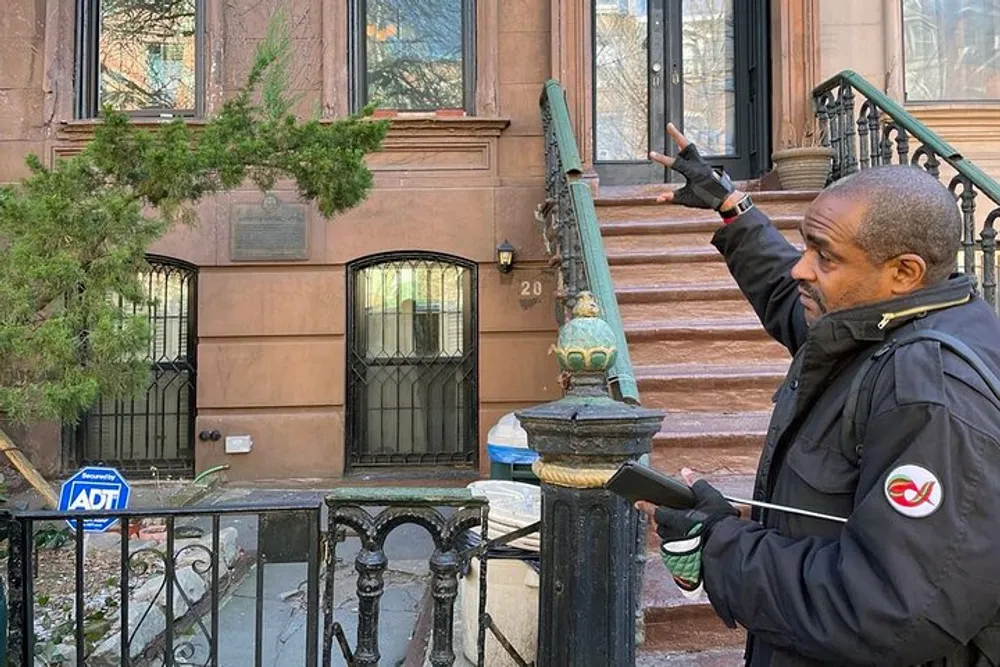 A person is pointing at a historical plaque beside the entrance to a brownstone building