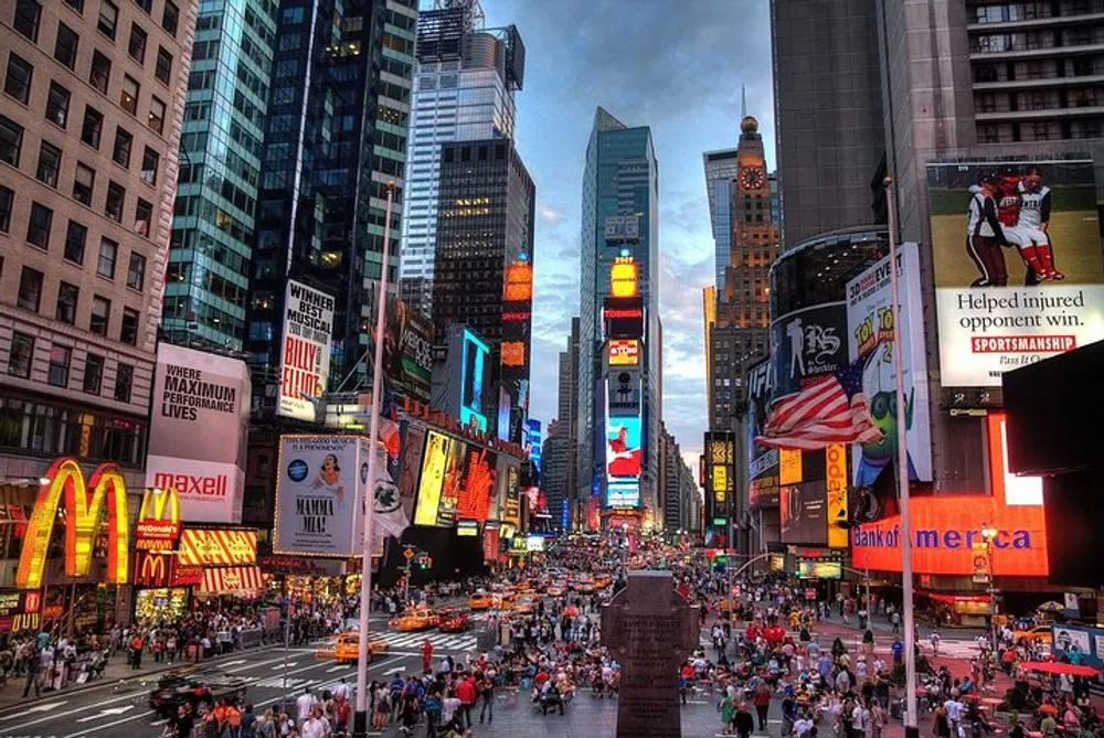 The image depicts a bustling Times Square in New York City with vibrant electronic billboards and a dense crowd of people