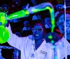 Two people wearing lab coats and safety glasses are working with glowing green chemicals in a laboratory setting