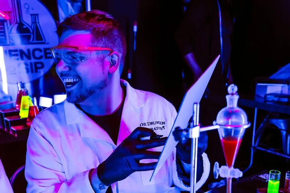 A person wearing protective eyewear is conducting an experiment or demonstration involving colorful liquids in a dimly lit lab-like setting with neon lights