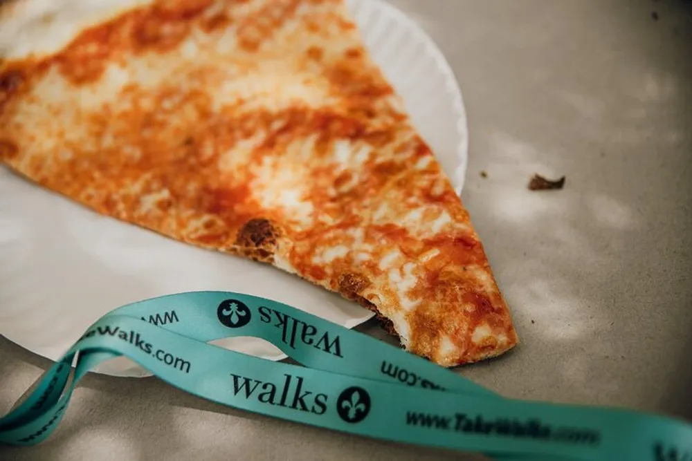 A single slice of cheese pizza rests on a paper plate beside a turquoise lanyard with the word walks printed on it