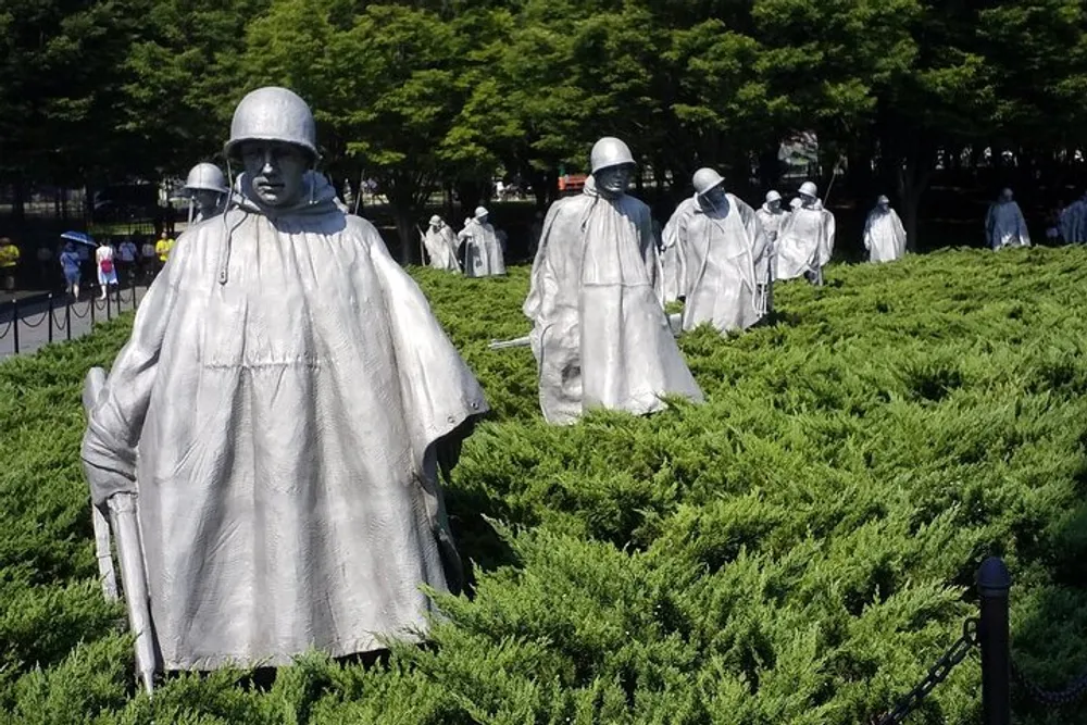 The image shows a group of statues depicting soldiers in uniform seemingly from the Korean War presented amidst greenery under a bright sky