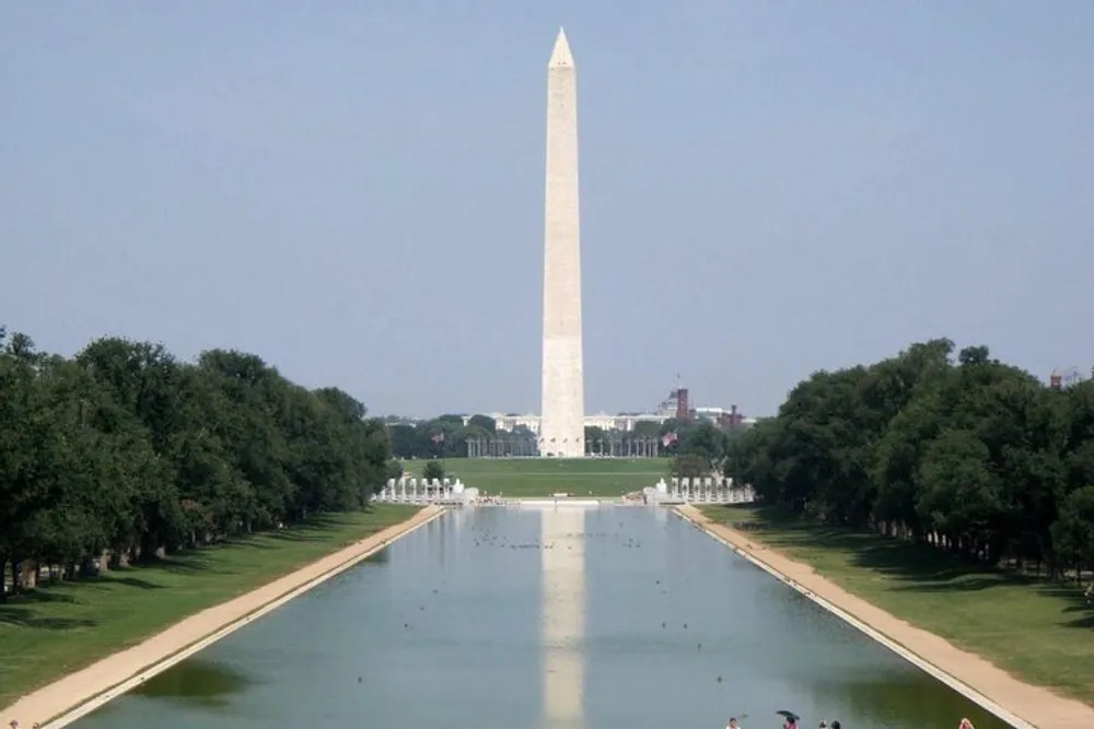 This image features the Washington Monument a towering obelisk overlooking the Reflecting Pool in the National Mall in Washington DC