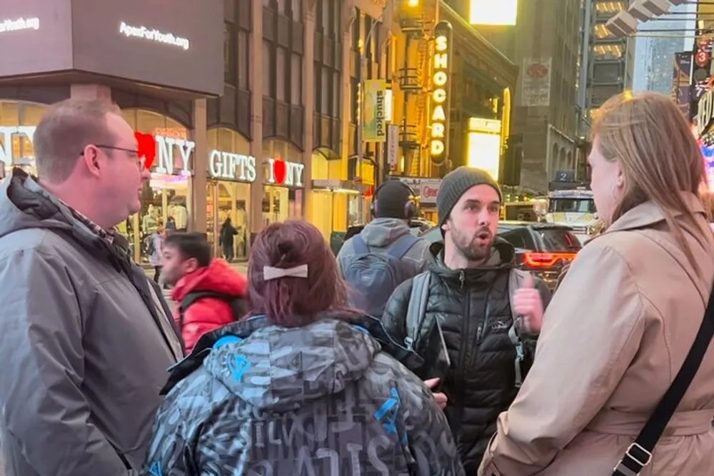 This image shows a group of people engaged in a conversation on a bustling city street with illuminated signs and storefronts in the background