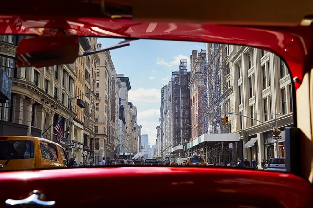 The image captures a bustling city street scene with buildings pedestrians and vehicles viewed from the inside of a red vehicle