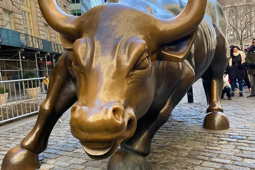 A bronze sculpture of a bull likely representing economic prosperity is observed closely by visitors on a paved street