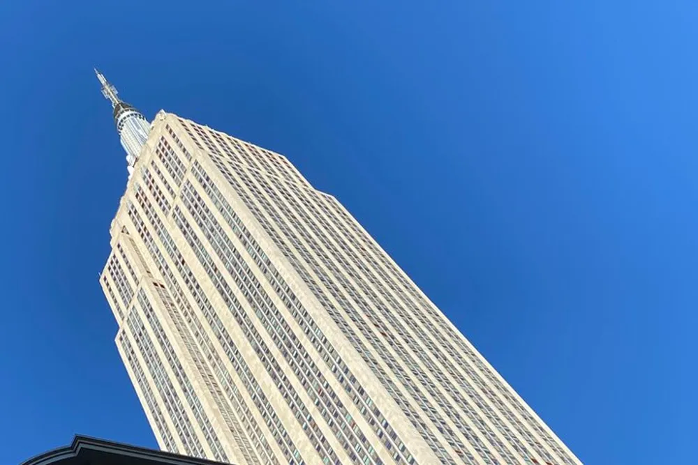 The image shows a worms-eye view of the Empire State Building against a clear blue sky