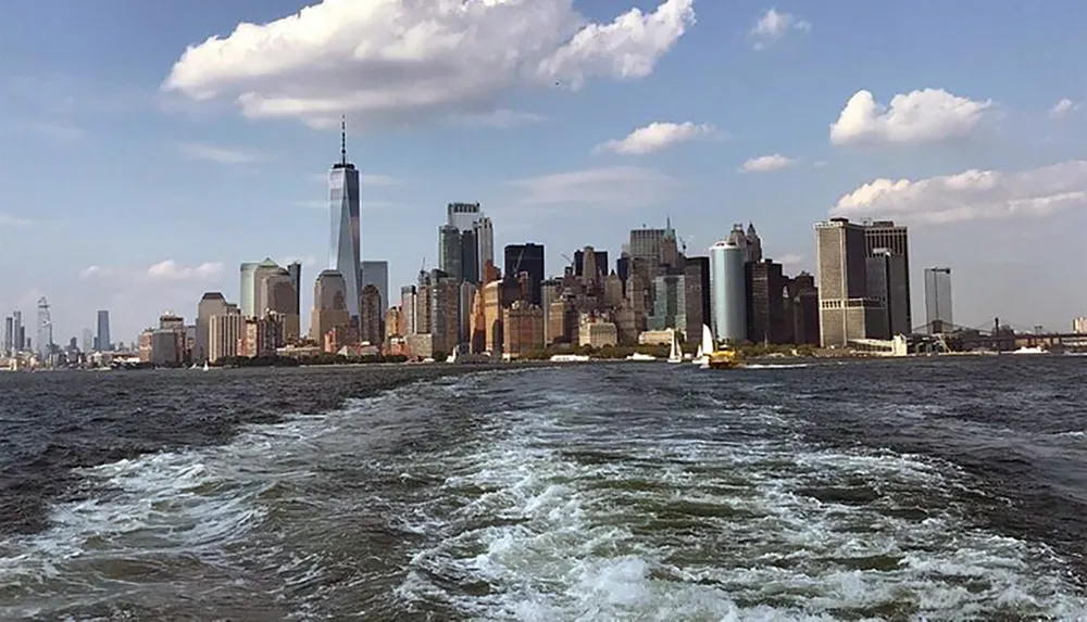 This image captures the Manhattan skyline seen from the water with prominent buildings and the wake of a boat in the foreground