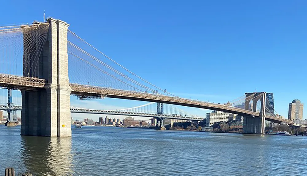 The image captures the Brooklyn Bridge spanning the East River with a clear blue sky in the background