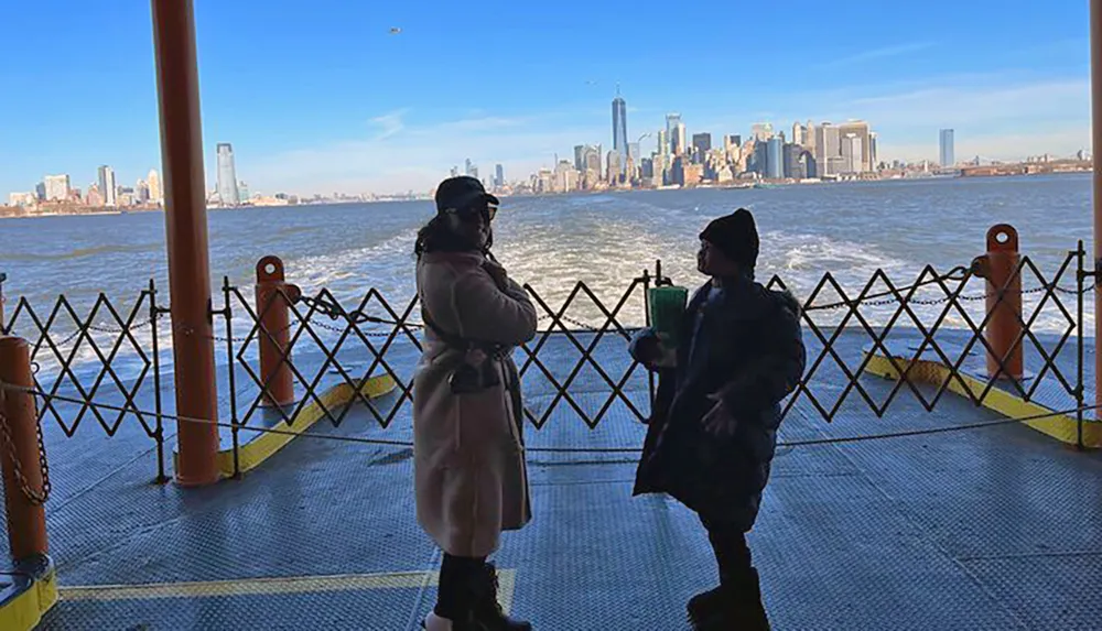 Two people are conversing on a ferry with the New York City skyline in the background