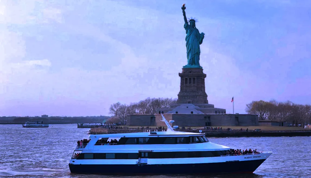 A ferry boat filled with passengers cruises near the Statue of Liberty under a cloudy sky