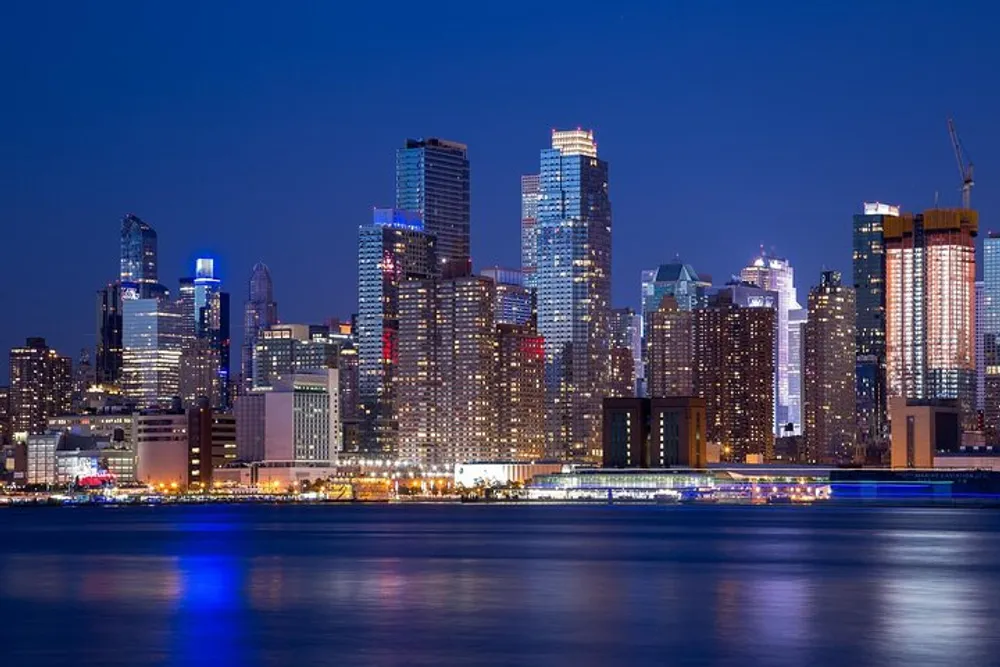 The image features a stunning skyline of illuminated skyscrapers at twilight with reflections on the water in the foreground