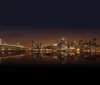 The image shows a nighttime view of a brightly lit city skyline possibly New York with skyscrapers and a bridge reflecting over the water